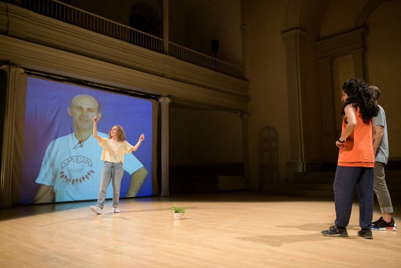 A woman dances in front of a projection of a man while people watch
